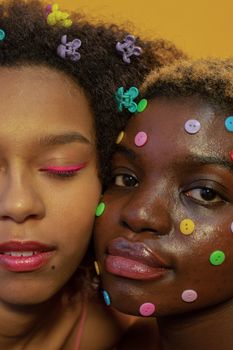 Crop African American female models with bright makeup and colorful buttons on face and multicolored vivid clasps in hair