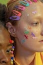 Crop unemotional multiethnic female models with bright multicolored stickers and fluffy balls on faces in studio