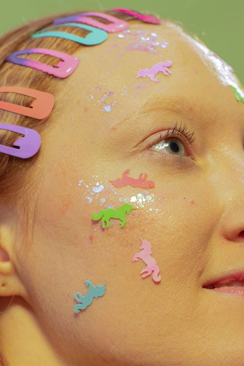 Crop positive female with vivid small stickers on face and multicolored hair clasps looking away against green background