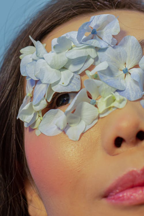 Crop Asian woman with blue petals on face