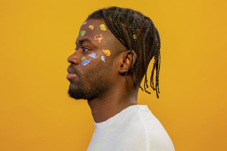 Trendy Young Black Guy With Multicolored Face Stickers Against Yellow Background