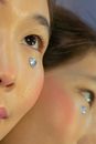 Crop unrecognizable Asian lady with natural makeup and rhinestone under eye holding mirror near face and looking up