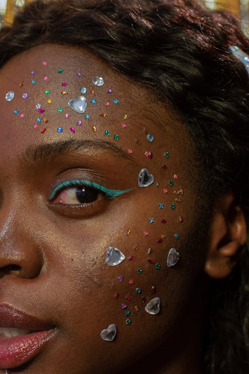 Crop attractive African American female with bright makeup and sparkling sequins on face looking at camera