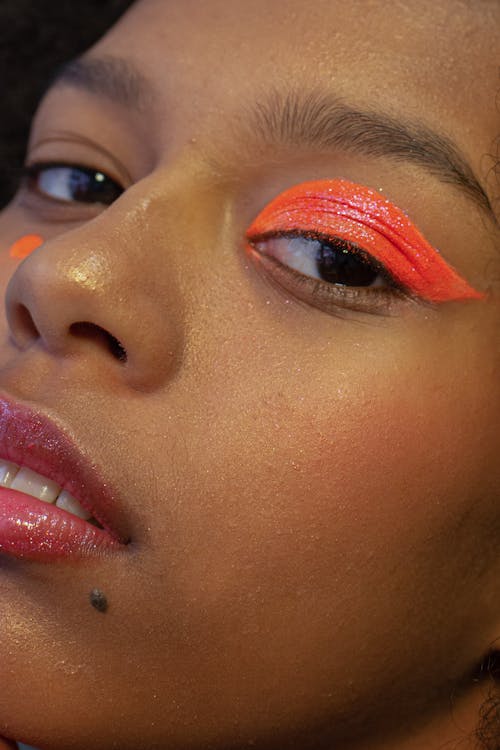 Free Crop beautiful African American female model with vivid orange eyeshadow on one eye looking at camera during photo shoot in studio Stock Photo