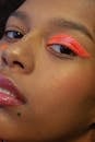 Crop beautiful African American female model with vivid orange eyeshadow on one eye looking at camera during photo shoot in studio