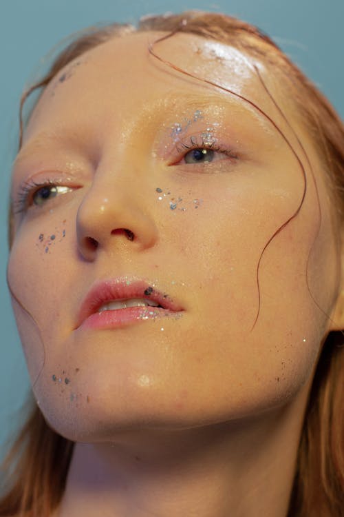 Emotionless female model with glitters and wet hair on face