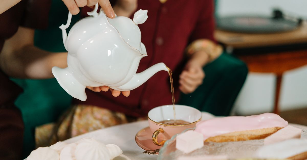 Close-up of pouring tea into a cup with elegant desserts, perfect for lifestyle themes.