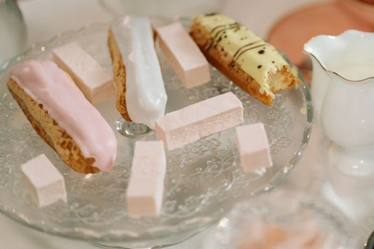 An elegant setup featuring eclairs and marshmallows on a decorative glass stand, perfect for dessert inspiration.