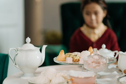 Free Child Sitting on the Table with Cookies and Tea Pot on It Stock Photo