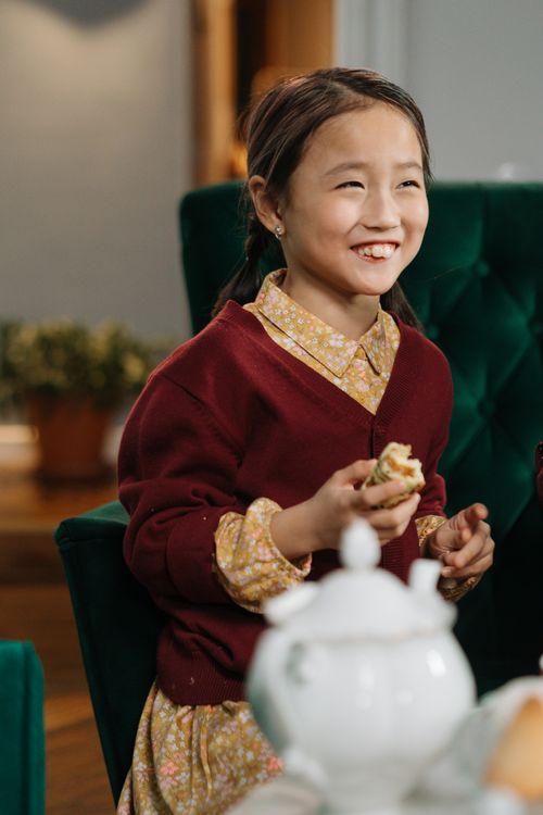 Free Happy child in floral dress enjoying tea indoors, capturing a joyful moment. Stock Photo