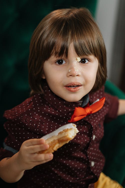 A Boy with Bread Crumbs on Face Holding an Icing Coated Bread with Crumbs