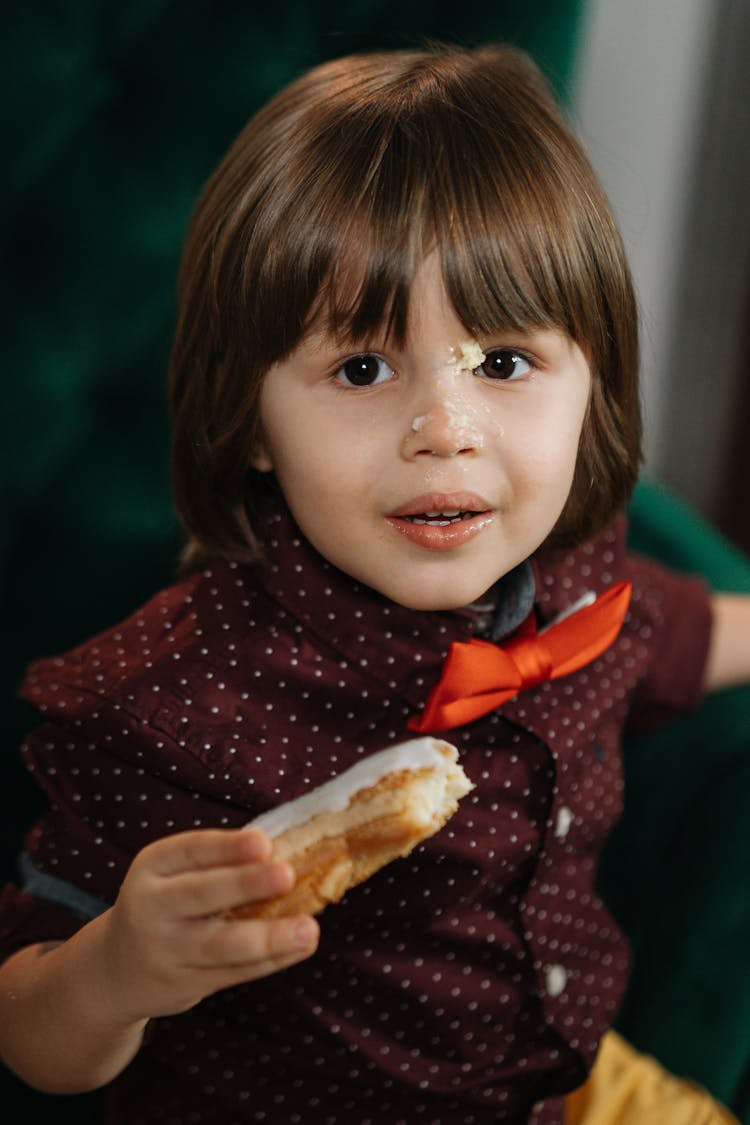 A Boy With Bread Crumbs On Face Holding An Icing Coated Bread With Crumbs