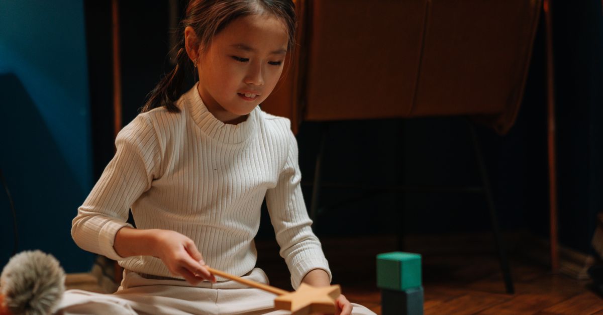 A girl plays with wooden toys on a wooden floor, creating a calm and focused scene.