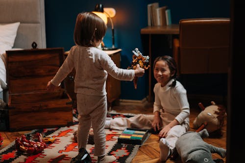 Free A Boy In Pajamas Showing a Plastic Toy to a Girl Sitting on the Floor Stock Photo