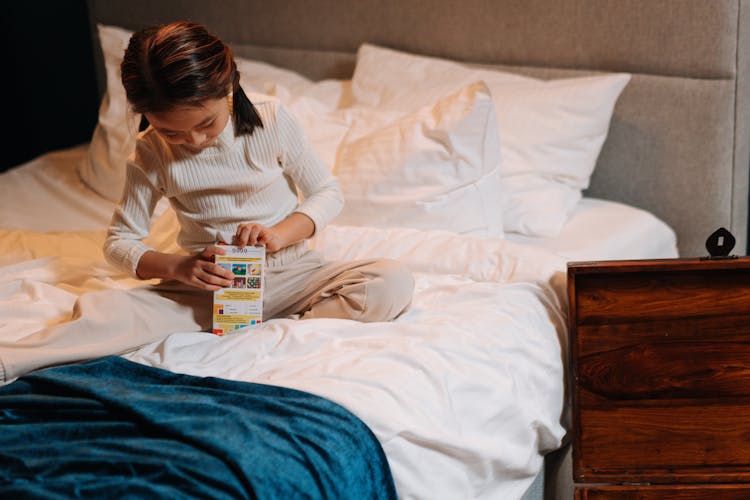 A Girl Sitting On A Bed Opening A Box