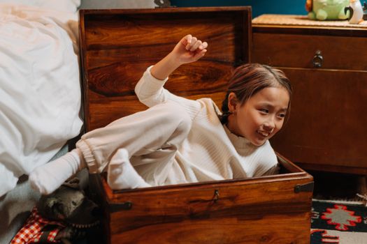 Smiling child enjoying playful moment inside a wooden chest indoors.