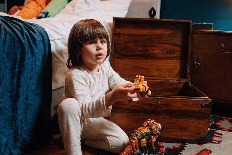 Child In Pajamas Holding A Toy Near A Bed