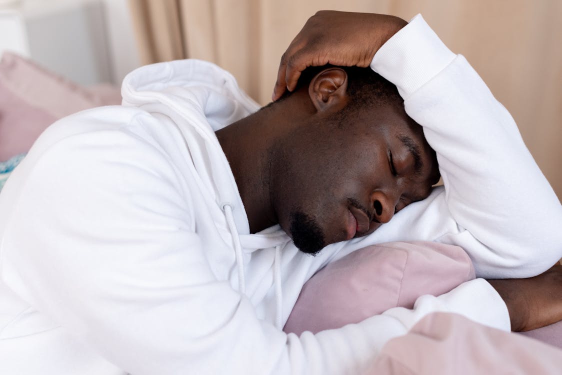 African American male with short dark hair in white hoodie leaning on hand and sleeping in light room