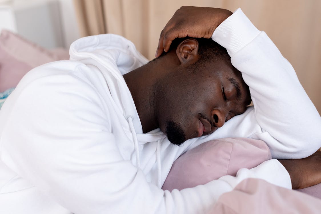 Free African American male with short dark hair in white hoodie leaning on hand and sleeping in light room Stock Photo