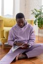 Black man reading magazine while sitting near sofa