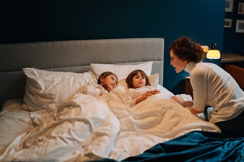 Free Woman Telling Story to Two Children in Bed Stock Photo