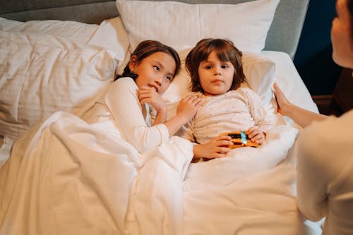 Free Children Listening to a Woman Sitting on the Edge of the Bed Stock Photo