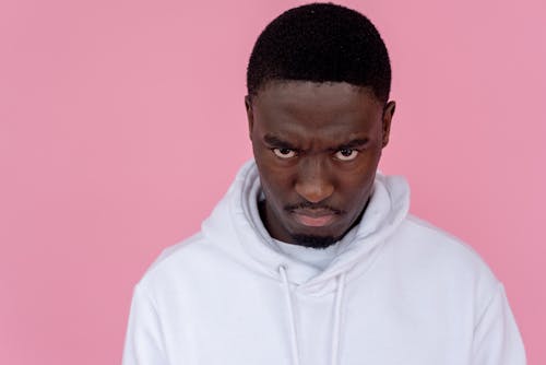 Angry black man in hoodie against light pink background