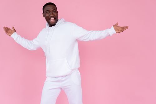 Free Happy African American male wearing white sweatshirt standing with hands outstretched against pink background and looking at camera Stock Photo