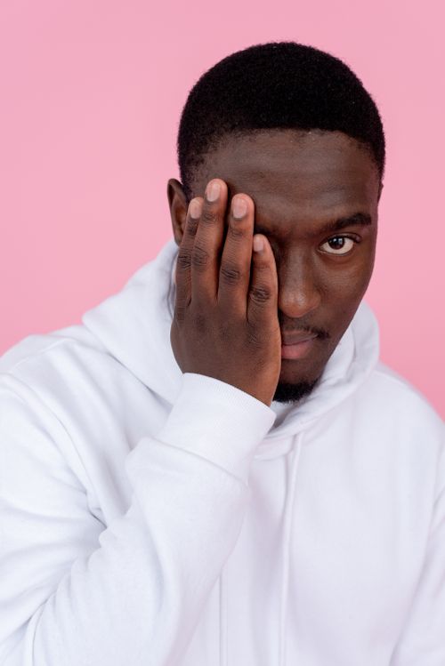 Free Confident African American male model wearing hoodie covering half of face with hand and looking at camera against pink background Stock Photo