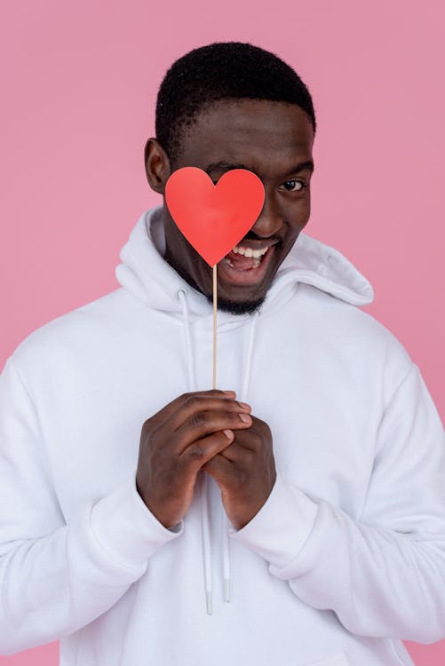 Cheerful African American male with heart smiling and looking at camera on pink background