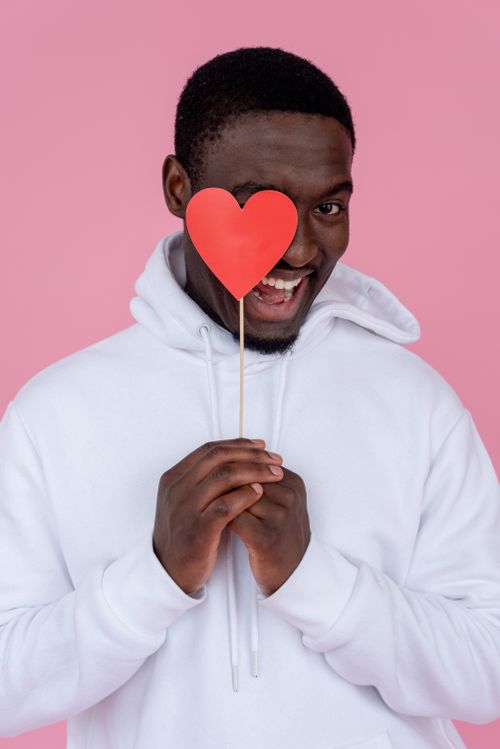 Free Cheerful African American male with heart smiling and looking at camera on pink background Stock Photo