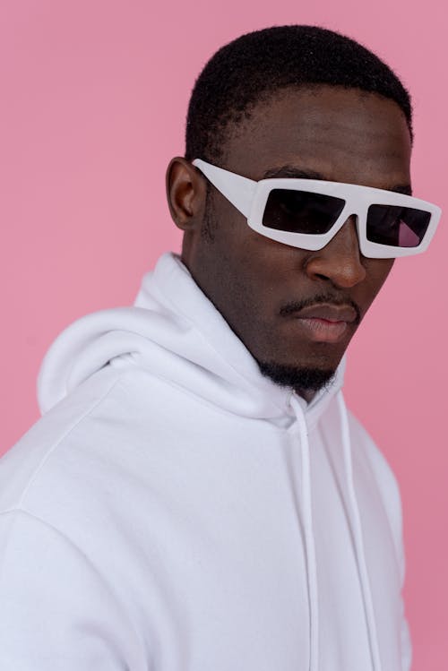 Free Serious young African American guy in white hoodie and sunglasses on pink background in bright studio Stock Photo