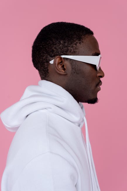 Side profile of a man with sunglasses and white hoodie against a pink backdrop.