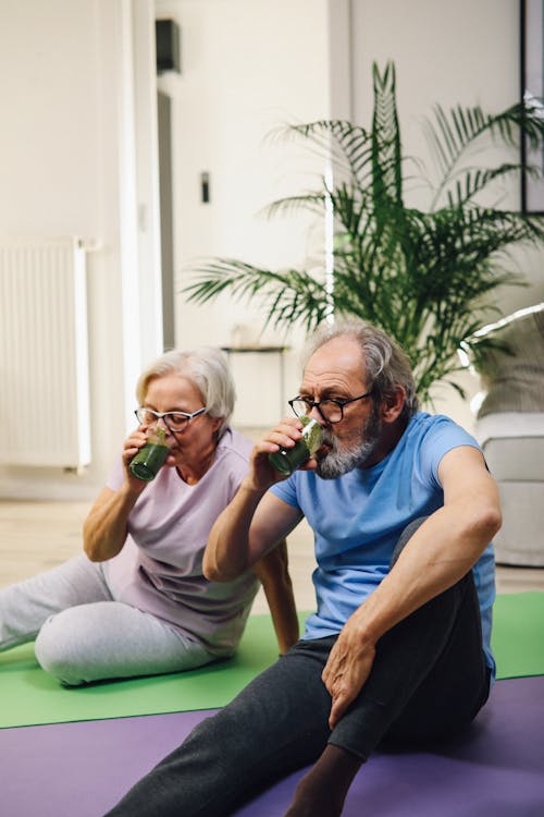 A Couple Sitting on Yoga Mats Drinking Green Juice