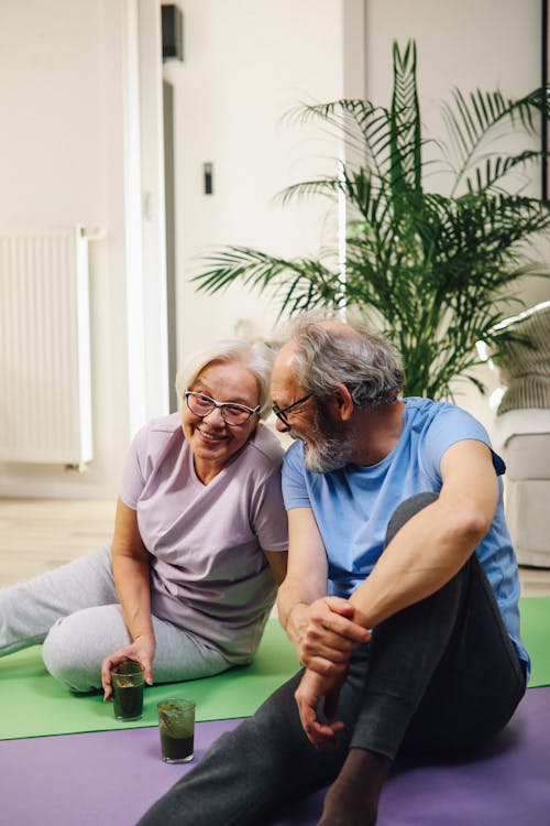 An Elderly Couple Sitting on Yoga Mats Smiling