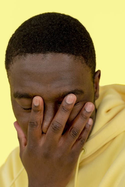 A Man in Yellow Sweater Covering His Face