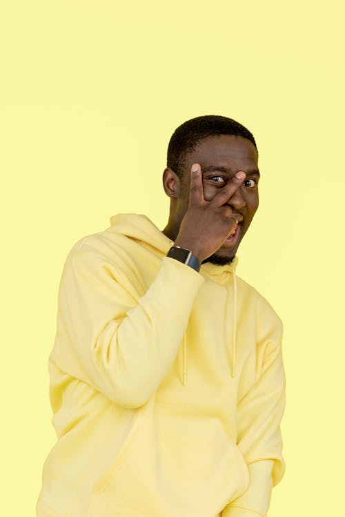 A Man in Yellow Sweater Doing Peace Sign with His Hand on His Face