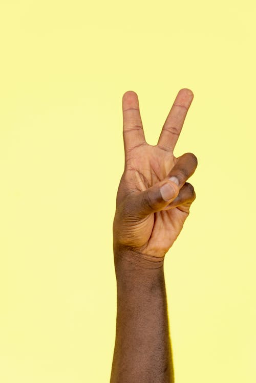 Kostenloses Stock Foto zu finger, friedenszeichen, gelbem hintergrund