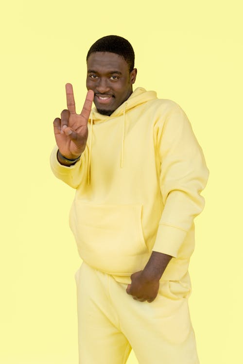 A Man in Yellow Hoodie Smiling while Doing Peace Sign