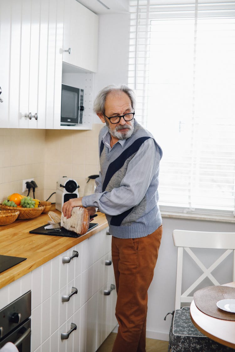 An Elderly Man Holding A Bread On The Kitchen While Looking Over Shoulder