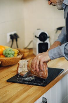 A man slices brown bread on a chopping board in a kitchen setting.