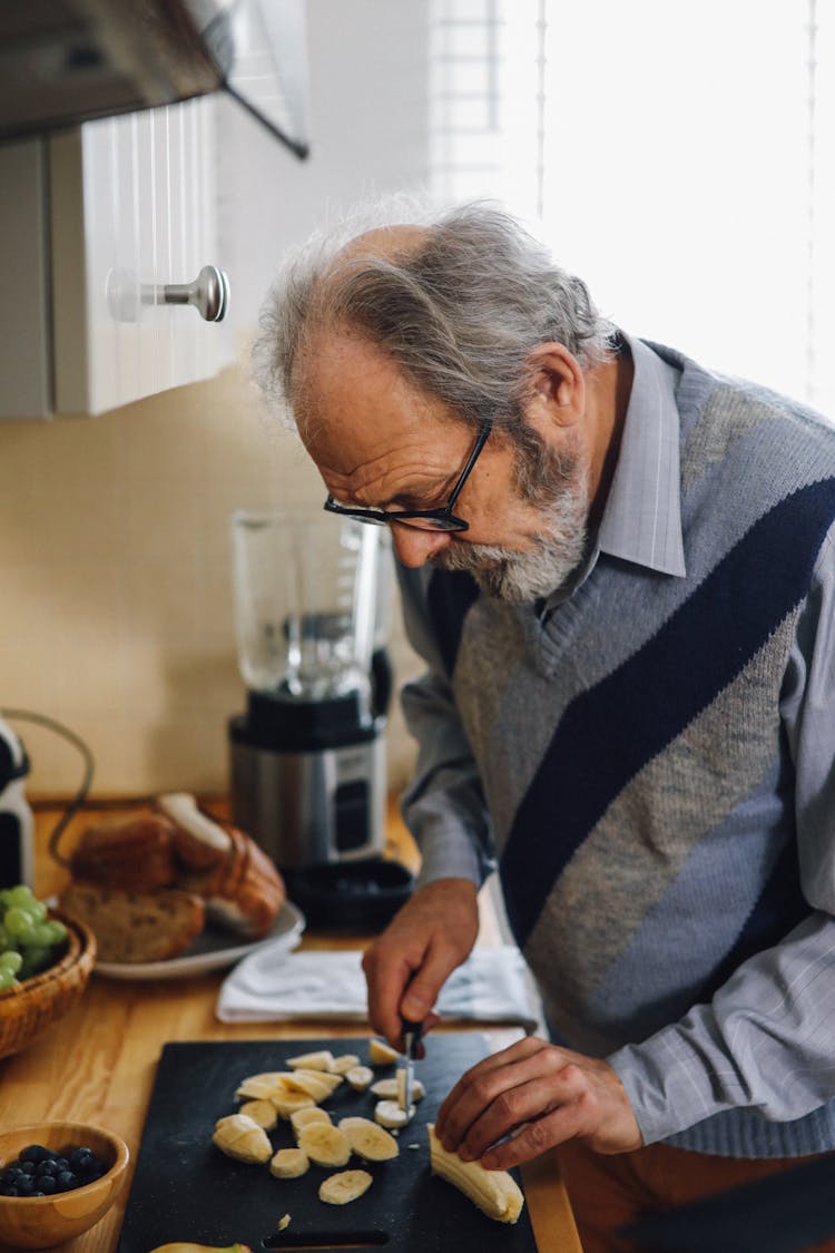 Elderly Man Slicing A Banana On A Chopping Board