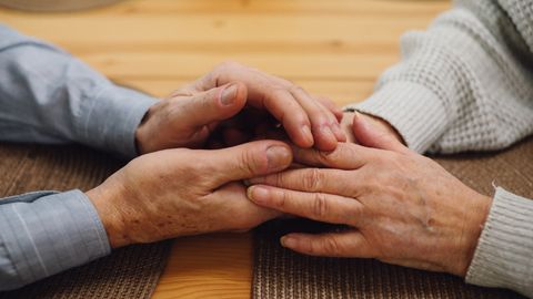A close-up of an elderly couple holding hands on a wooden table, signifying love and companionship.