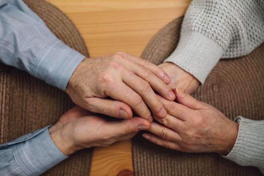 Mãos de familiares e cuidadora unidas sobre a mesa