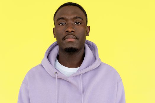 Close-up portrait of a man wearing a purple hoodie against a vibrant yellow background with neutral expression.