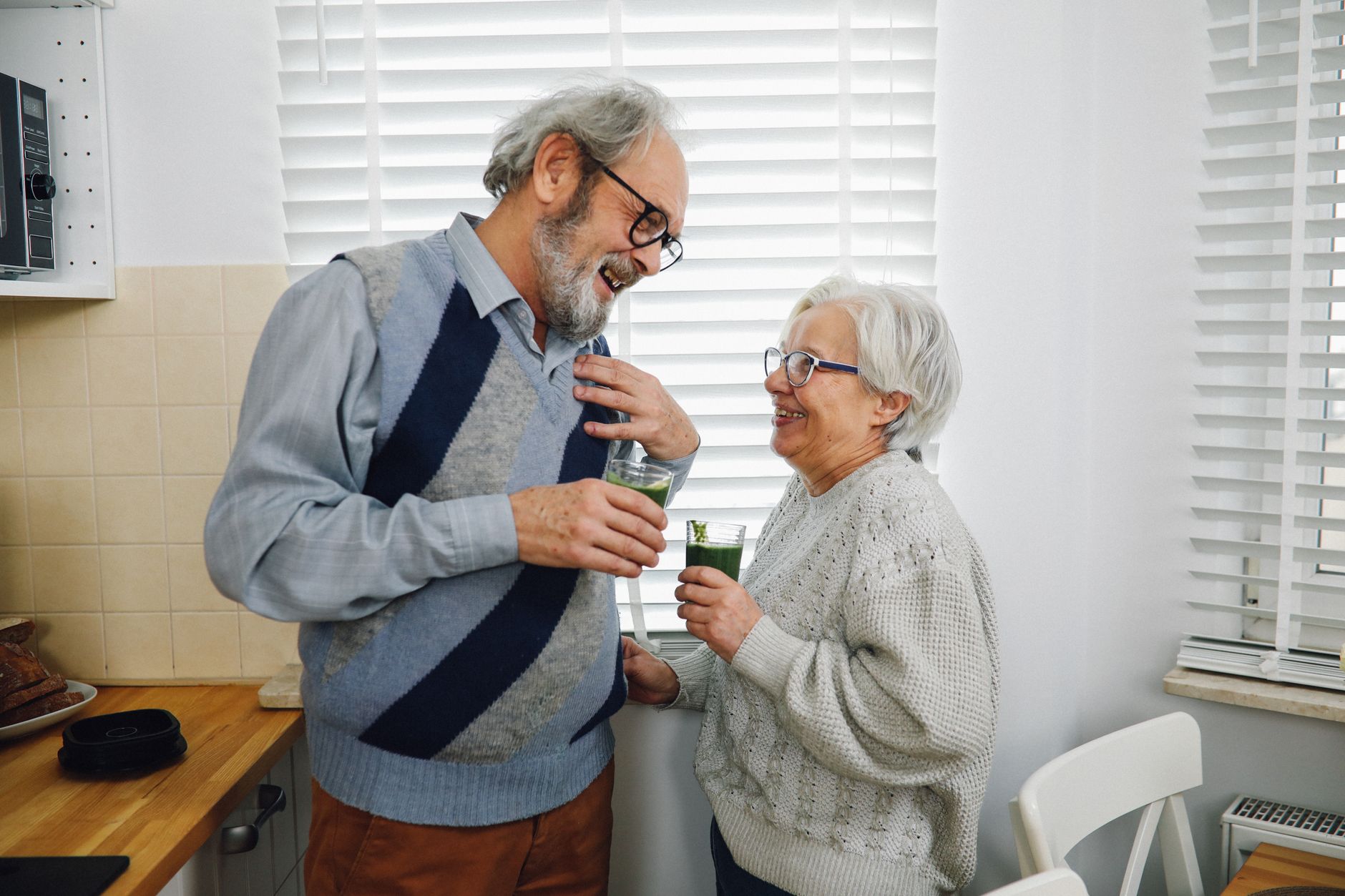 longevity protocol book — Elderly couple smiling and holding drinks in a cozy kitchen setting.