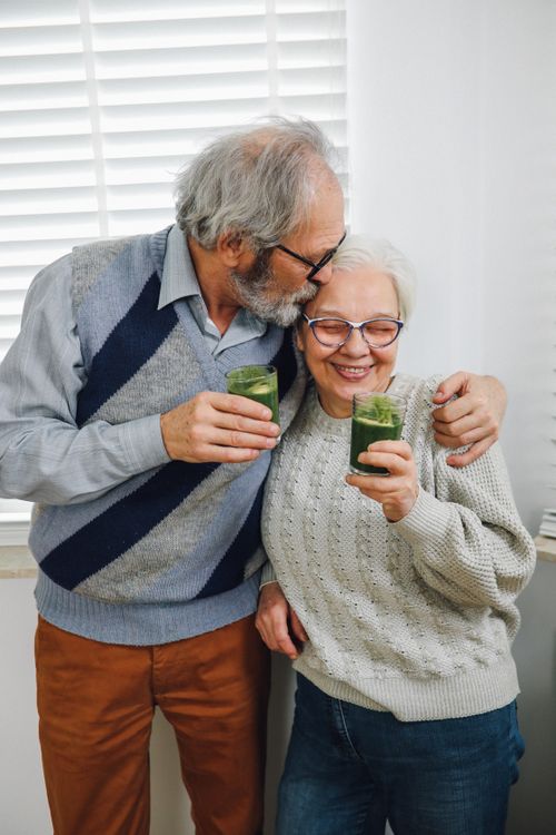 Free Happy elderly couple sharing a moment with healthy green smoothies indoors. Stock Photo