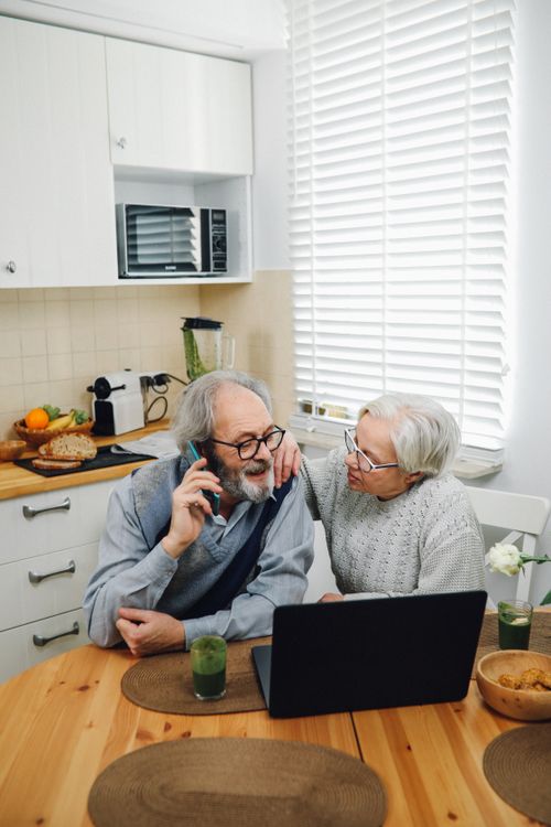 Free Elderly couple enjoying technology at kitchen table, using laptop and phone. Stock Photo
