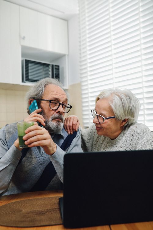 Free Elderly couple engaged with laptop and phone in a cozy kitchen environment. Stock Photo