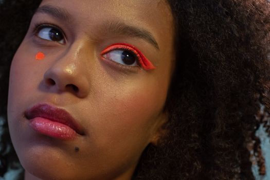 Crop unemotional African American female with bright orange eyeshadow on one eye looking away in studio